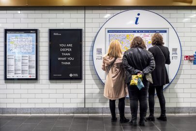 People look at a sign on the tube, a poster by Laure prouvost next to them reads 'you are deeper than what you think'