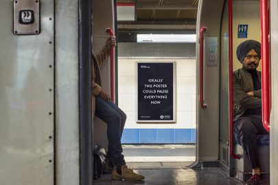 A poster by Laure Prouvost is seen through the open door of a busy train, it reads 'ideally this poster could pause everything now'