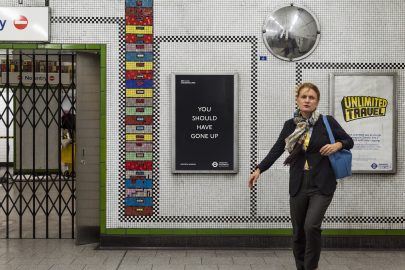 A poster by Laure Prouvost reads 'you should have gone up' as a women walks by in a tube station