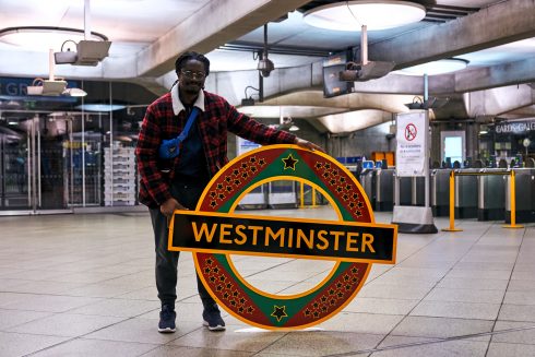 Larry Achiampong with his new permanent artwork for Westminster station, 'PAN AFRICAN FLAG FOR THE RELIC TRAVELLERS’ ALLIANCE (UNION)', 2022. Courtesy the artist and Copperfield, London. Photo: Reece Straw, 2022